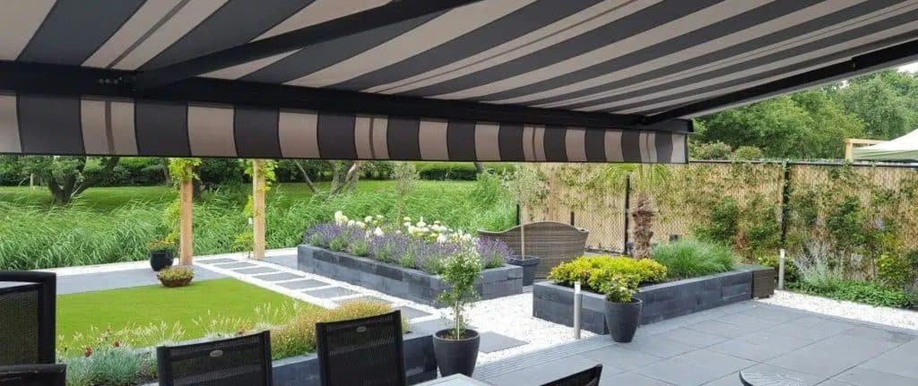 op deze foto is een mooie tuin te zien met een terras met daarboven een knikarmscherm van wullems zonwering